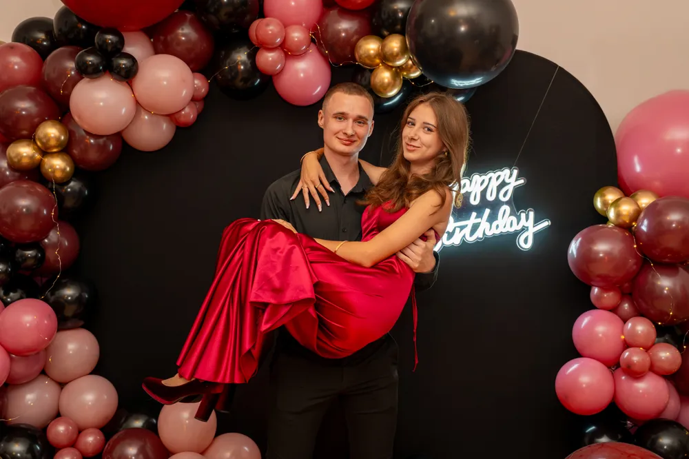 Para na osiemnastce przed łukiem balonowym i neonem Happy Birthday