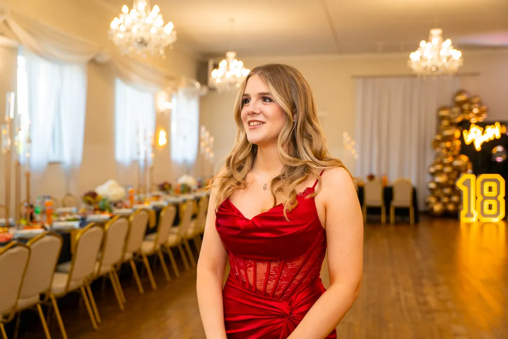 Jubilatka w czerwonej sukni w eleganckiej sali z żyrandolami i podświetloną liczbą 18